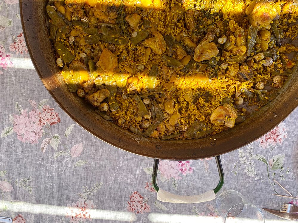 Traditional Valencian paella in a large pan, prepared with chicken, rabbit, green beans, and snails, placed on a floral-patterned tablecloth.