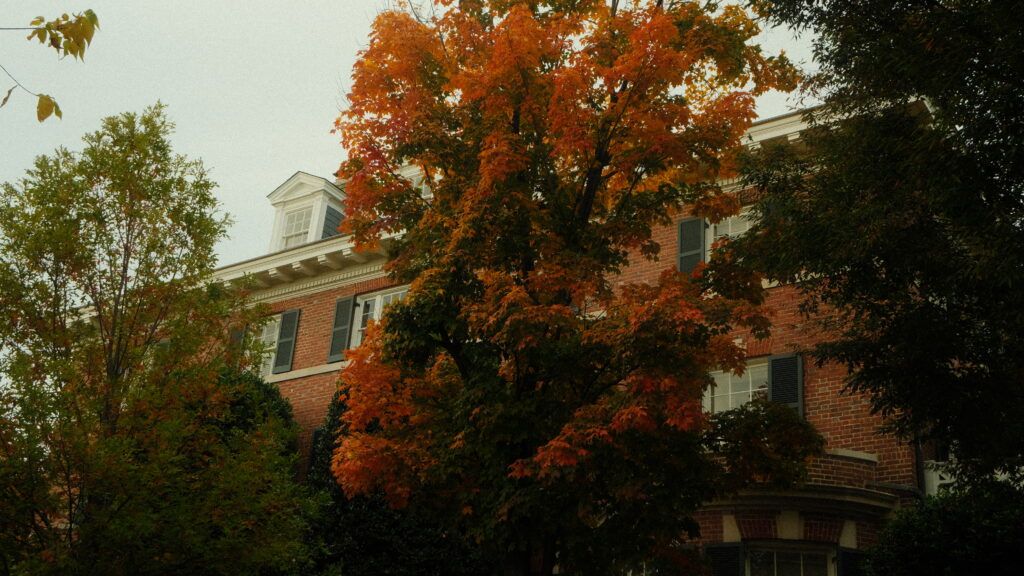 Brick residential building partly hidden behind trees with autumn foliage in shades of orange and green