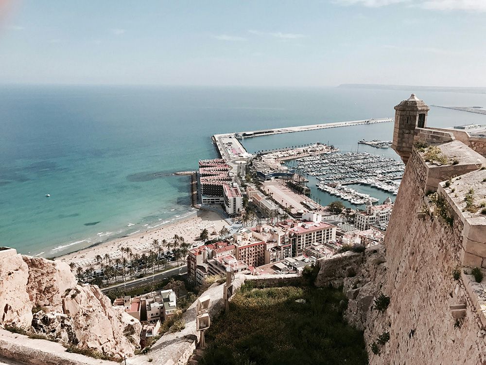 Wide angle image of Alicante Spain's coastal city. The ocean and old town is visisble showcasing the striking architecture and vivid blue sea.