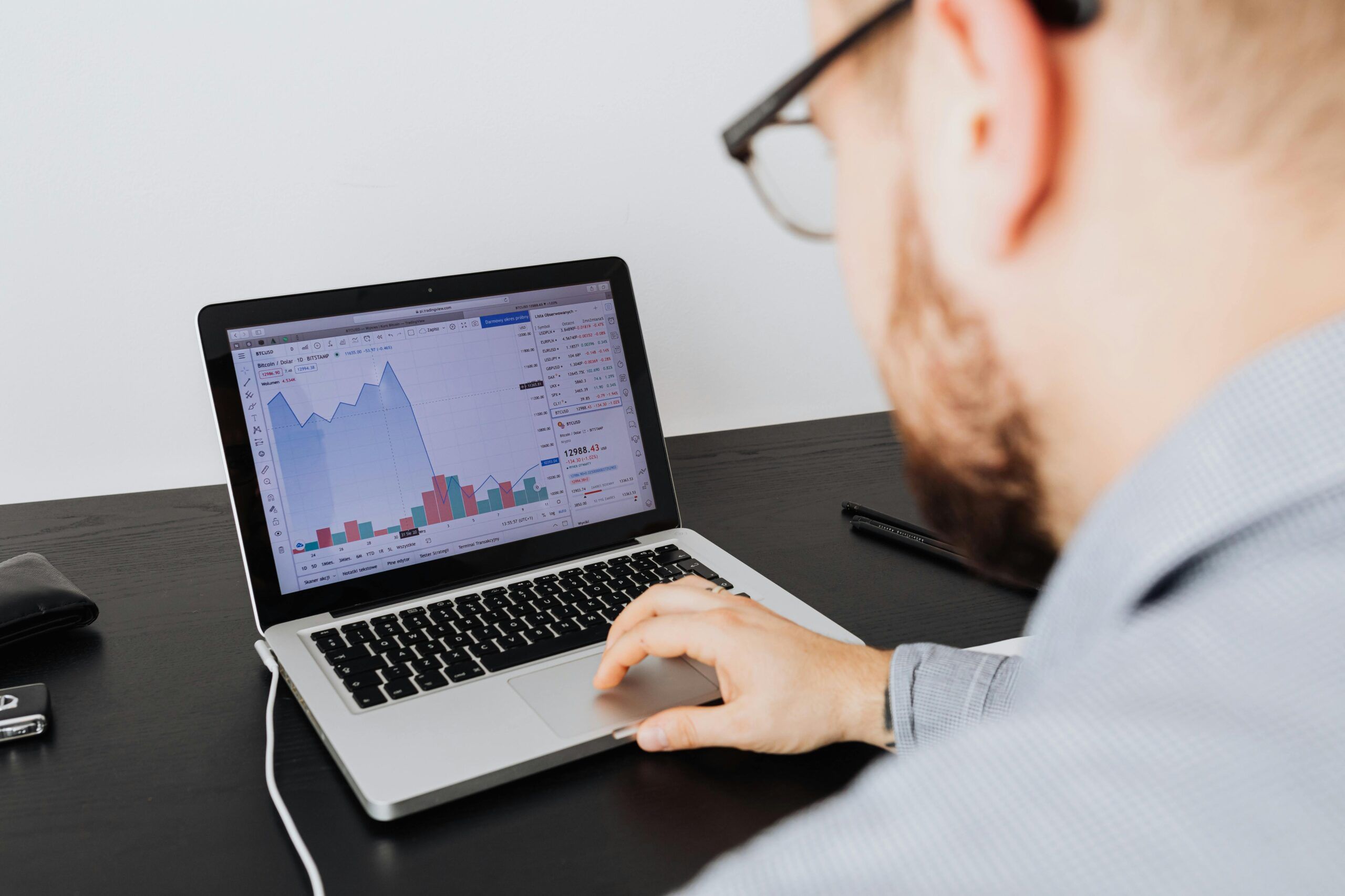 Man analyzing financial charts and bar graphs on a laptop screen at a desk