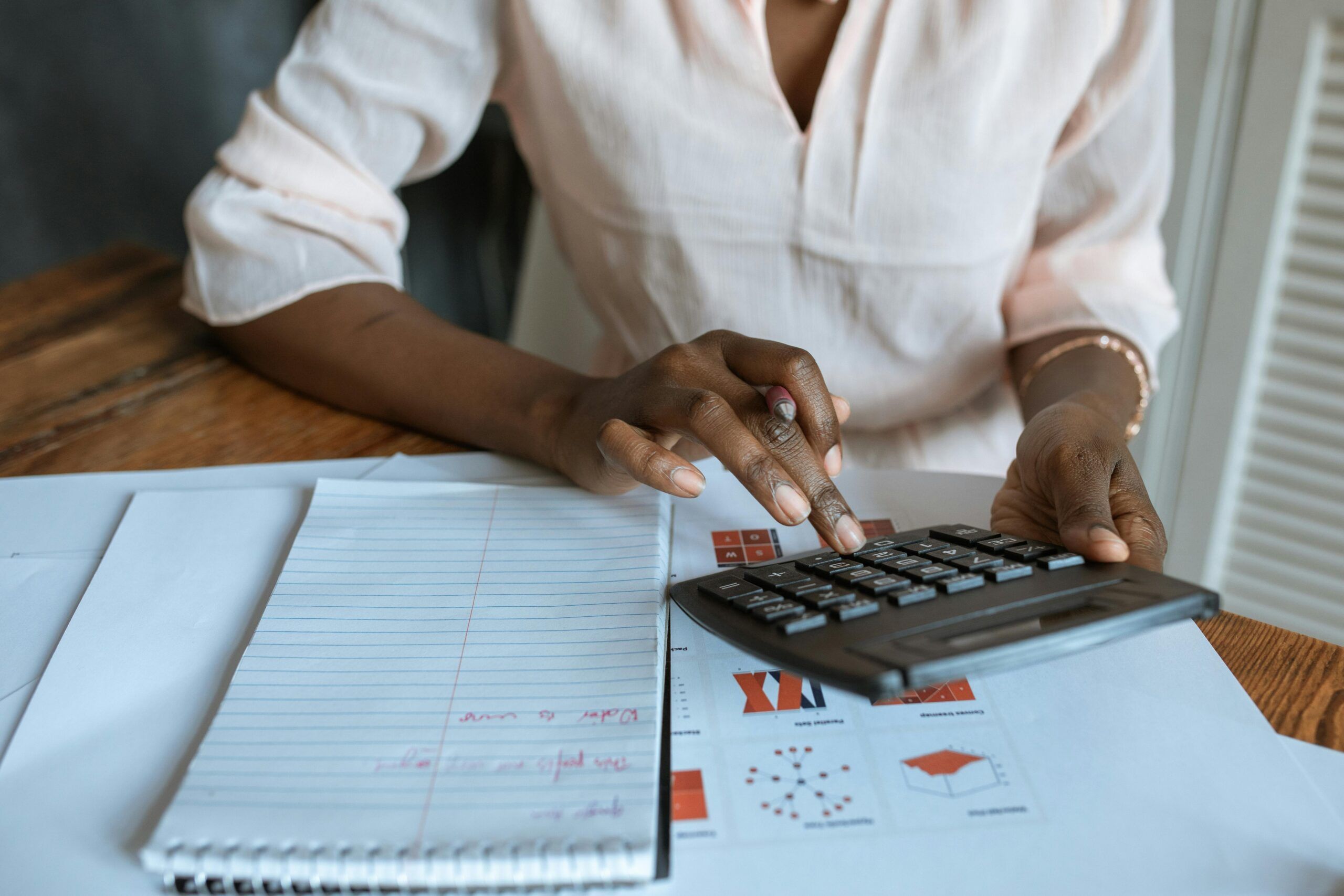 Close-up of a woman using a calculator at a desk with financial documents and a notebook.