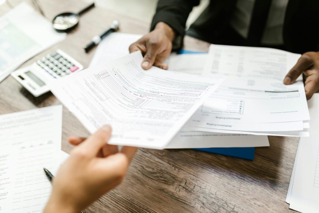 Close-up of people reviewing financial documents and tax forms at a desk with a calculator.