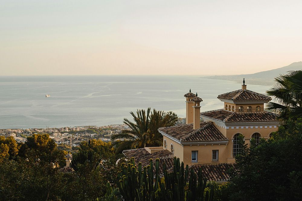 Mediterranean hillside villa with terracotta roof overlooking the sea and coastal city at sunset.