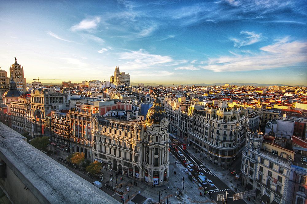 Panoramic view of central Madrid with historic buildings, the Metropolis building, and a wide city skyline under a blue sky with clouds.