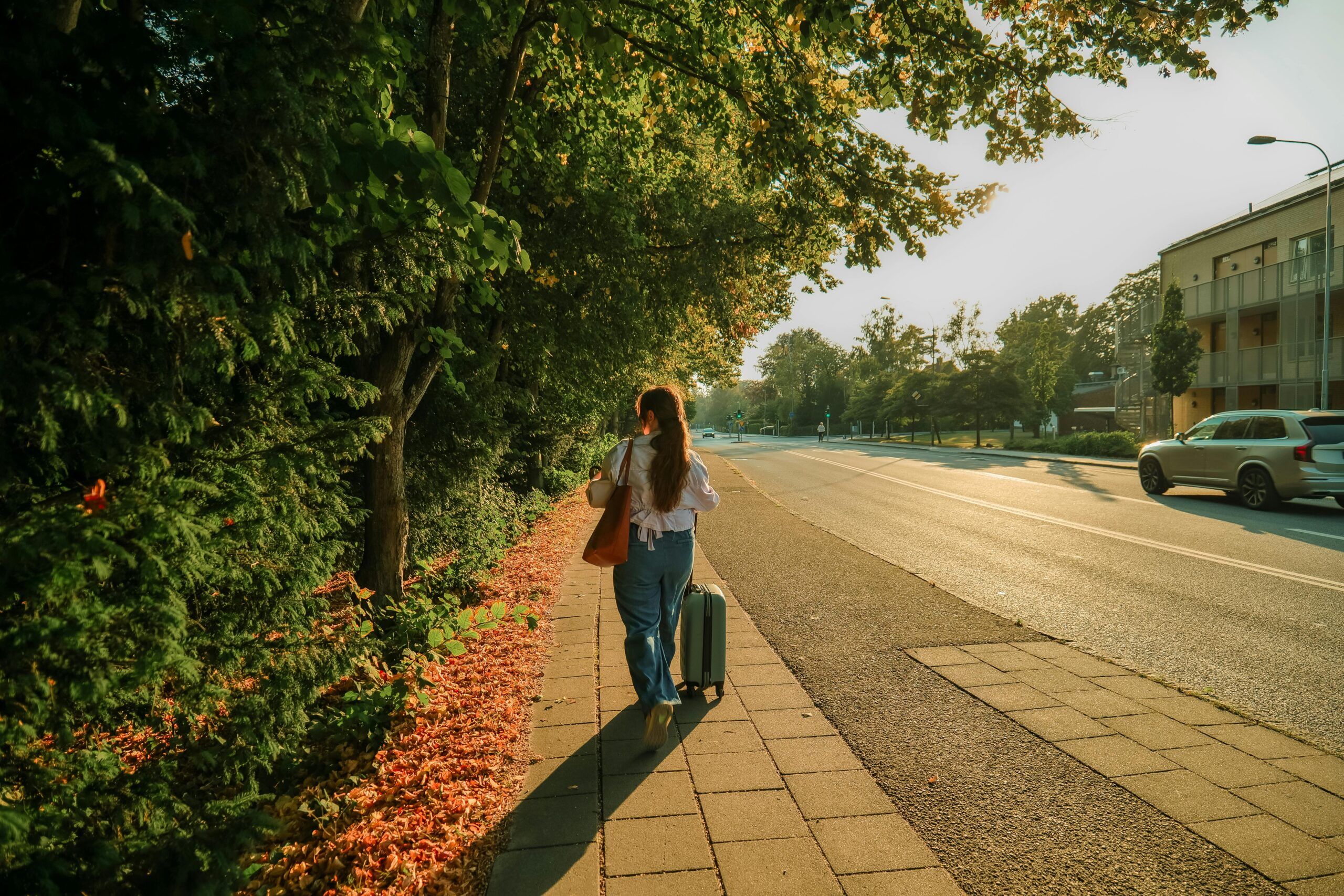Woman walking along a tree-lined street in autumn with a suitcase, symbolizing expats moving to Spain