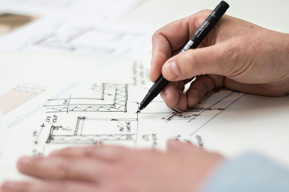 Close-up of a person’s hand drawing architectural sketches with a black pen on technical paper.