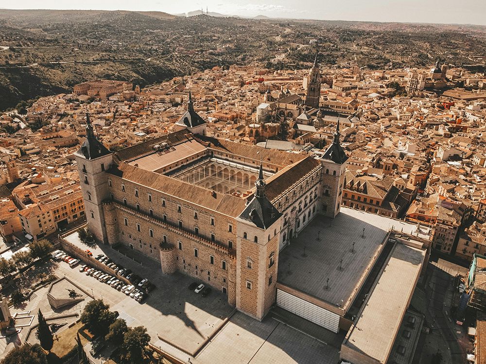 Aerial view of Toledo, Spain, with the Alcázar fortress prominently overlooking the historic cityscape.
