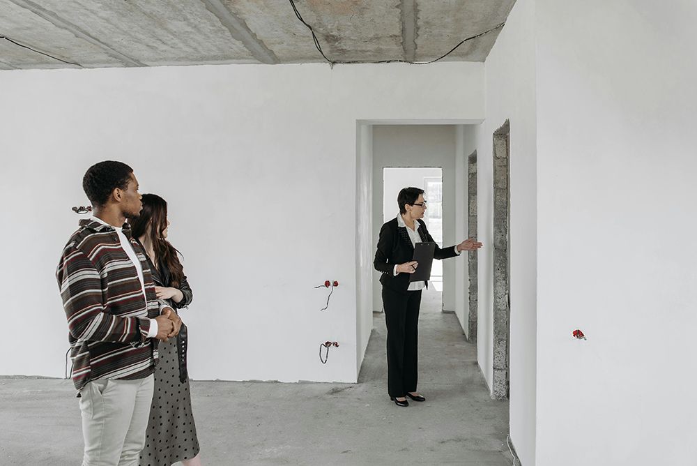 Real estate agent showing an unfinished apartment to a couple, discussing potential renovations and layout options.