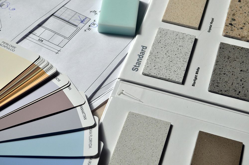 Selection of paint color swatches and stone countertop samples laid out on top of architectural drawings, showing options for home renovation or interior design.