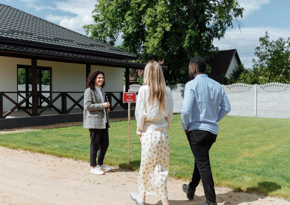 Real estate agent showing a house for sale to potential buyers on a sunny day in Spain.