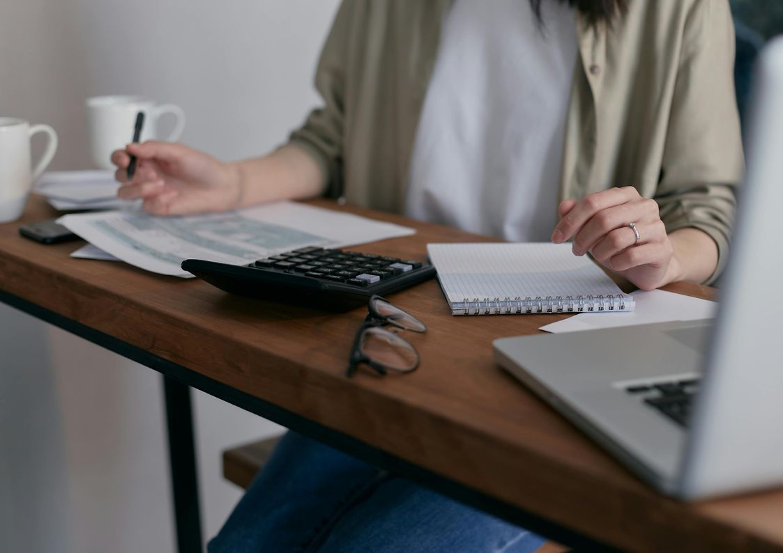 A person reviewing financial documents at a desk with a calculator, notebook, and laptop while planning property taxes.