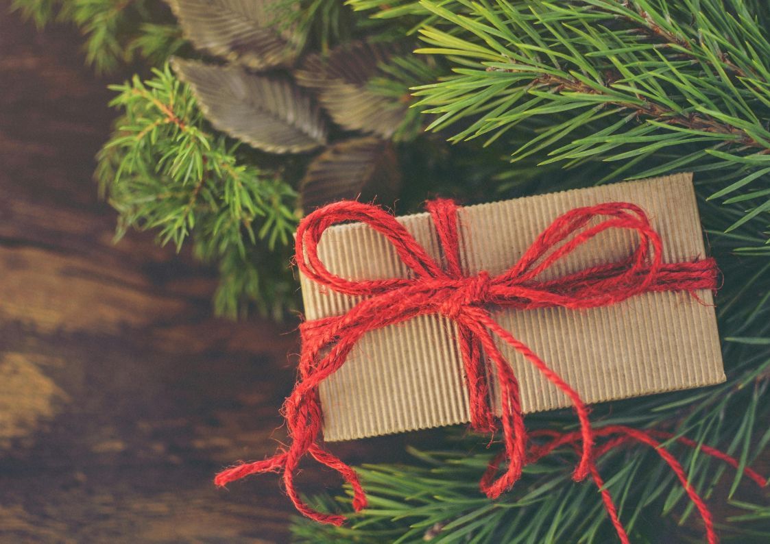 Christmas gift wrapped in brown paper with a red bow placed among festive pine branches.