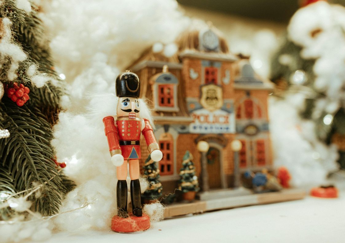 A festive nutcracker figurine displayed beside Christmas village decorations and faux snow.