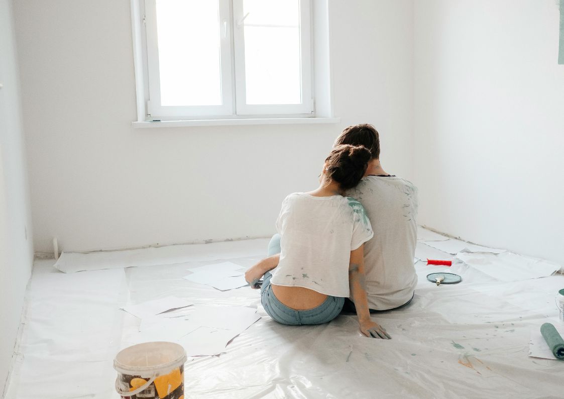 Couple sitting on the floor of a newly renovated room, leaning on each other while planning home updates.