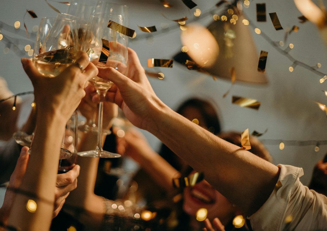 Group of friends raising glasses in a festive New Year’s celebration with confetti.