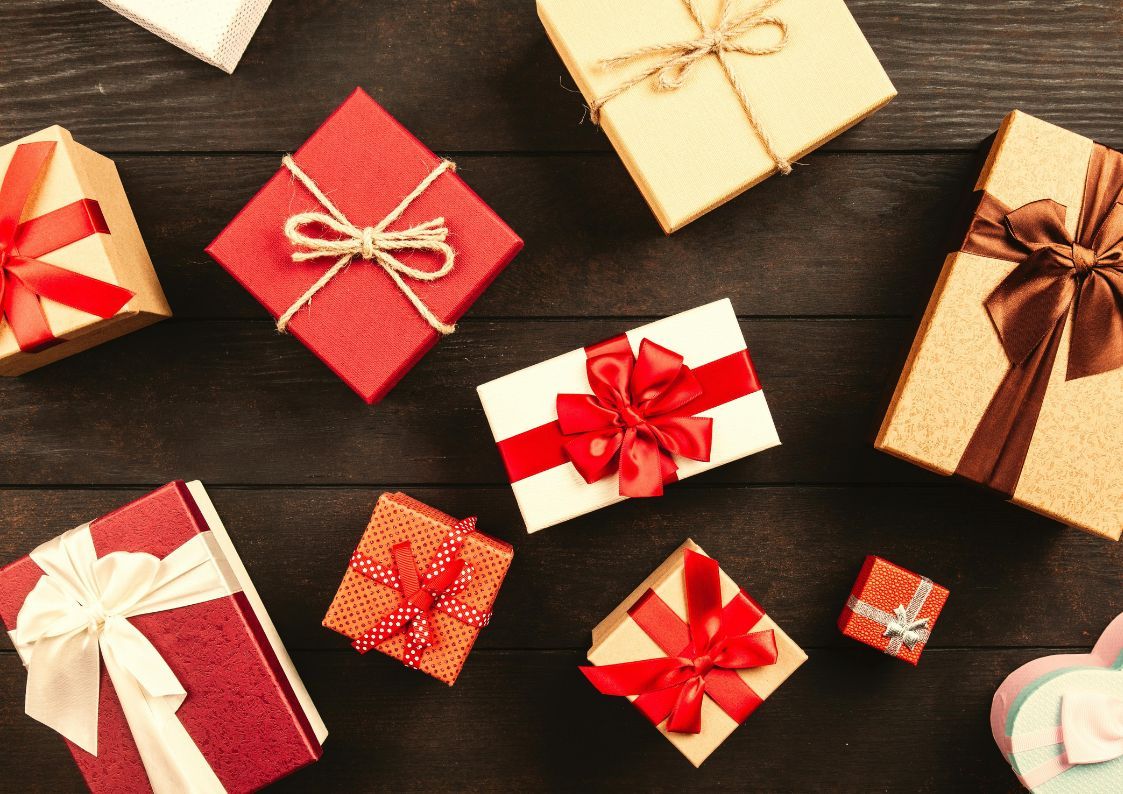 Assorted Christmas presents wrapped with red and gold ribbons arranged on a wooden table.