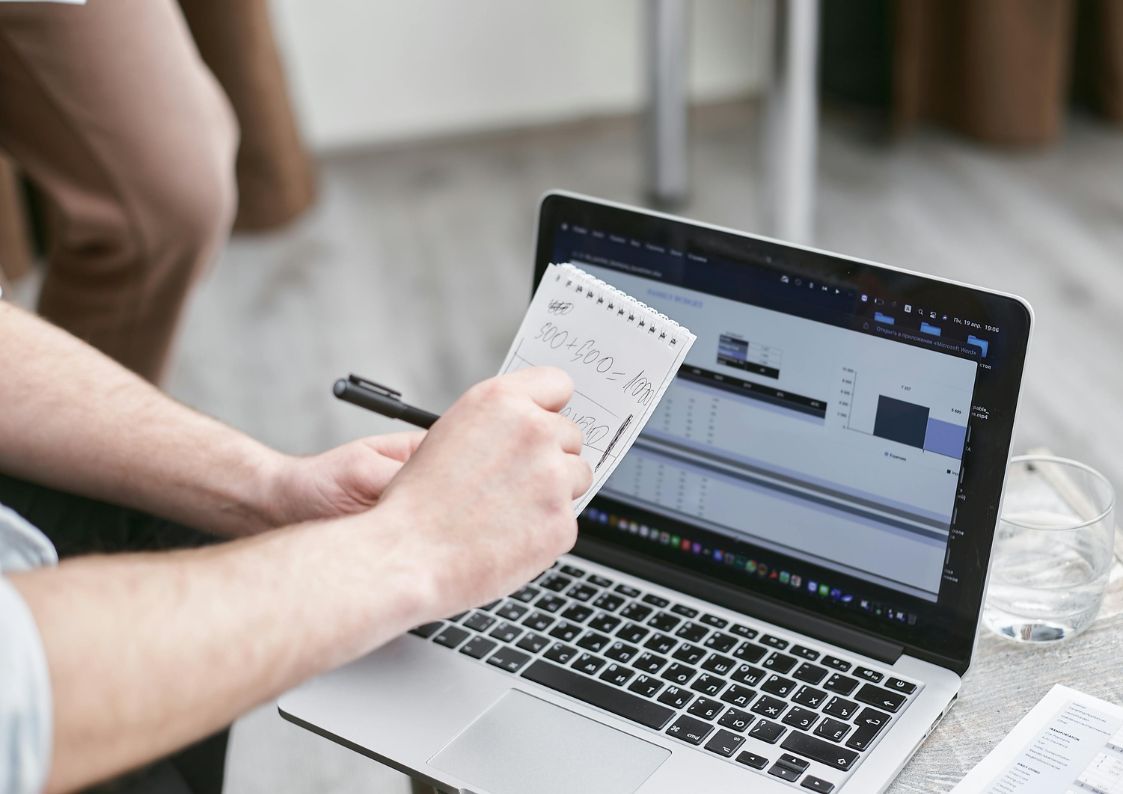Investor reviewing financial charts and notes on a laptop for real estate market analysis.