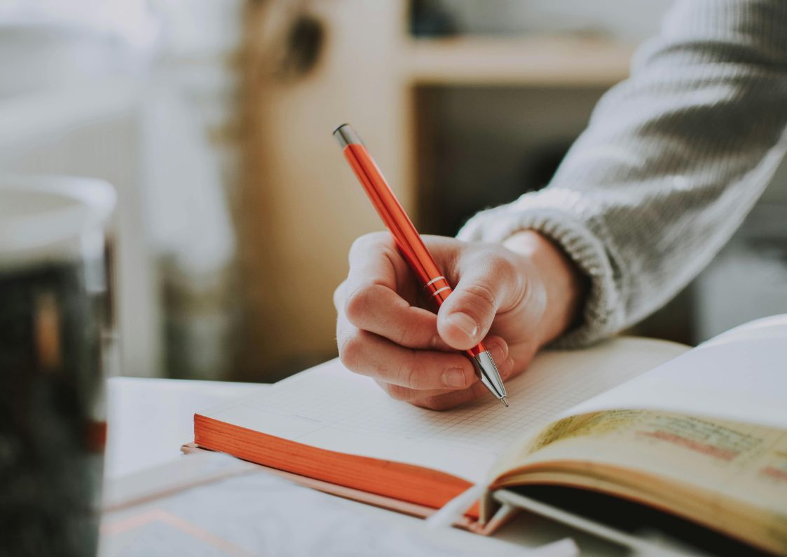 Hand writing investment goals in a notebook with a red pen at a cozy home workspace.