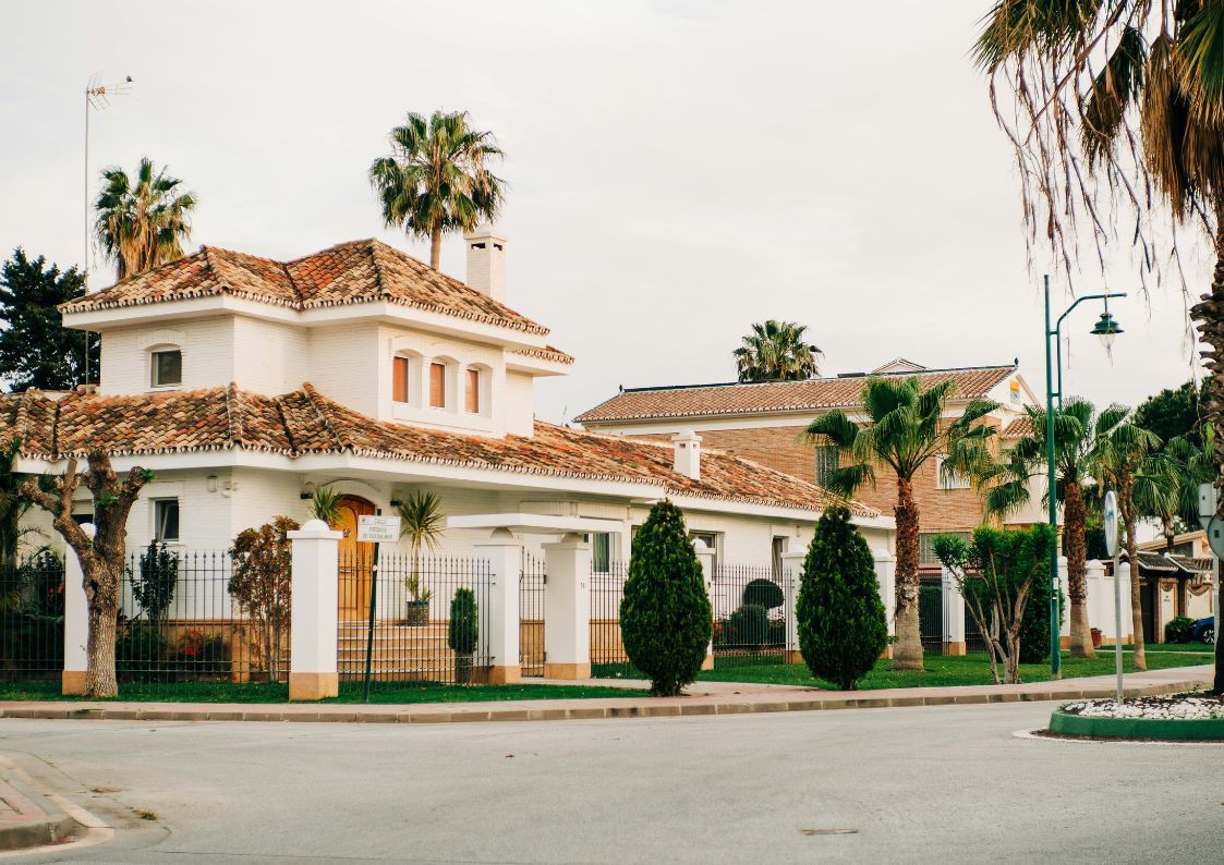 White Mediterranean villa with tiled roof and palm trees in a quiet Spanish residential neighborhood.