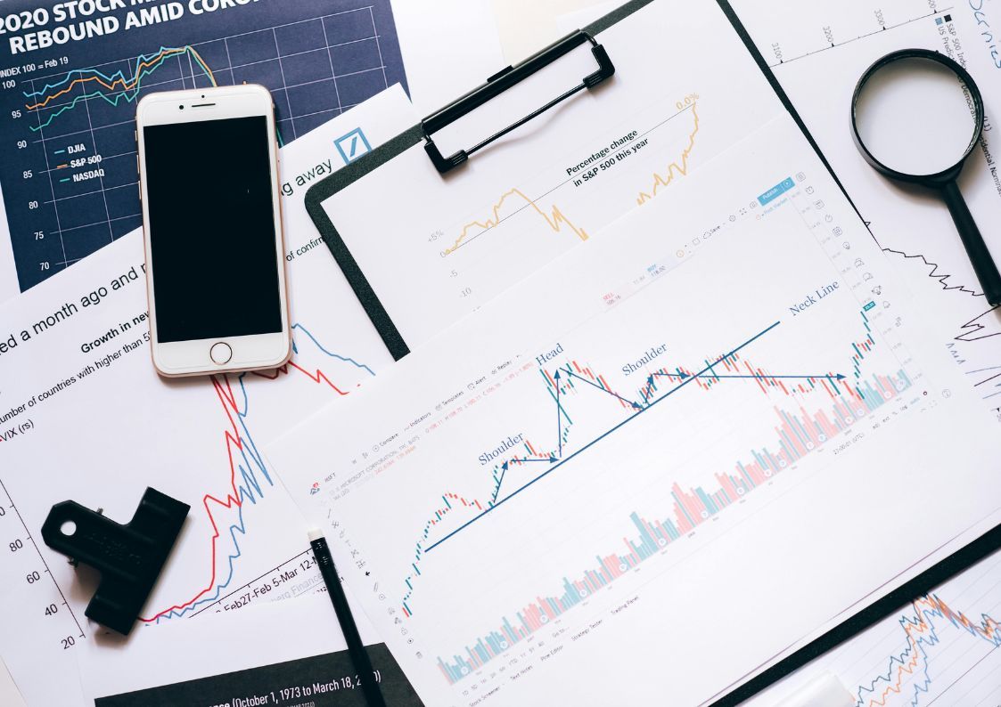 Financial charts, smartphone, and documents showing market trends and investment analysis.