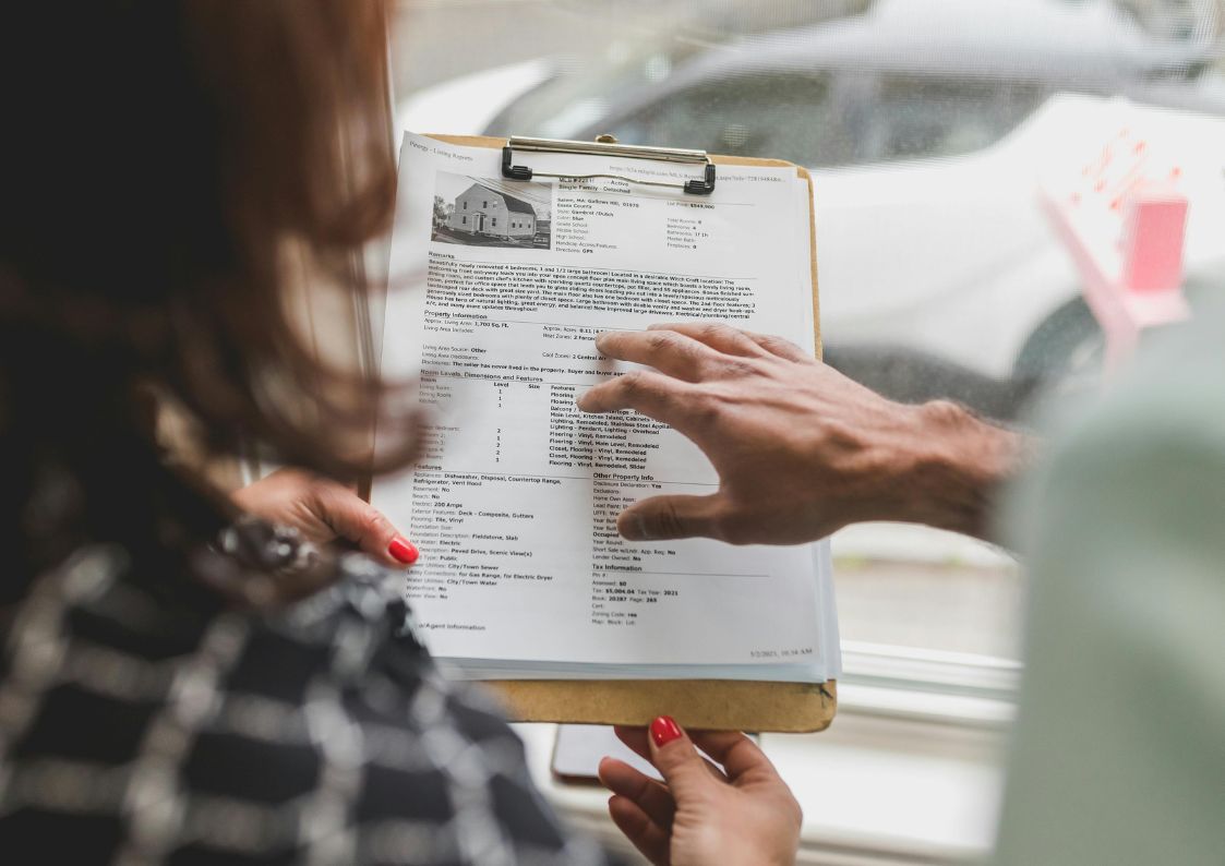 Real estate agent showing a property listing checklist to a client near a window.