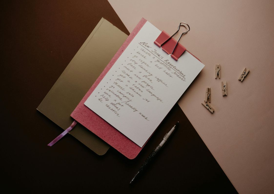 Notebook with handwritten New Year’s resolutions clipped to a folder on a desk.