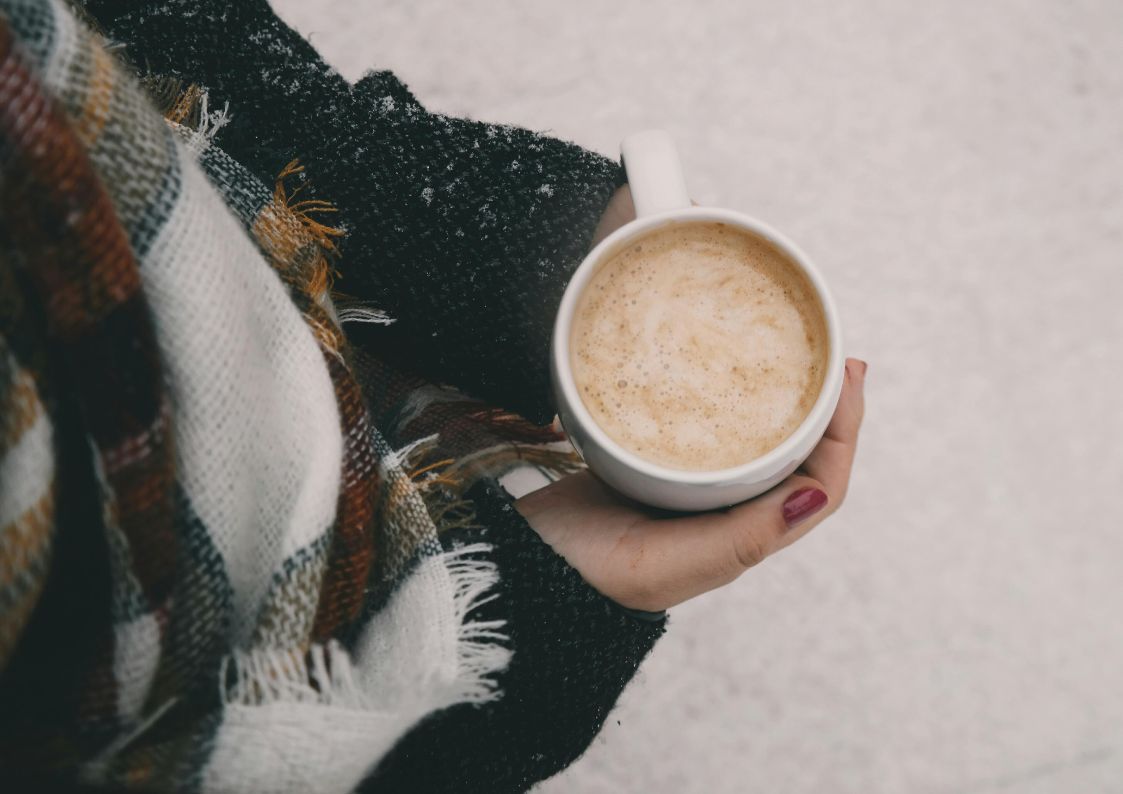 Person holding a warm coffee outdoors in winter, wrapped in a scarf on a cold day