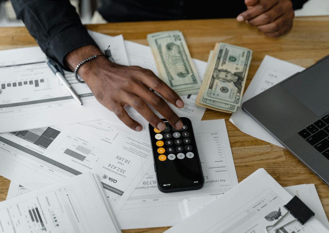 Person calculating finances with a calculator, cash, and paperwork, representing budgeting and financial planning for living or investing in Spain.