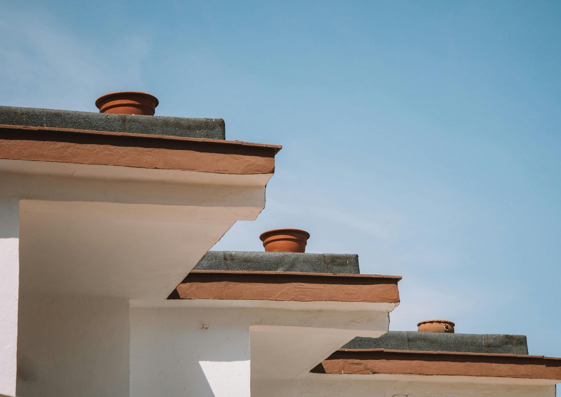 White Spanish rooftops with terracotta chimney pots under a clear blue sky, showcasing traditional Mediterranean architecture.