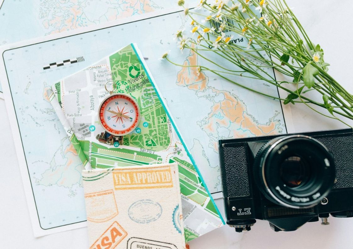 Travel documents, maps, and a camera on a table, representing planning a move to Spain and visa preparation
